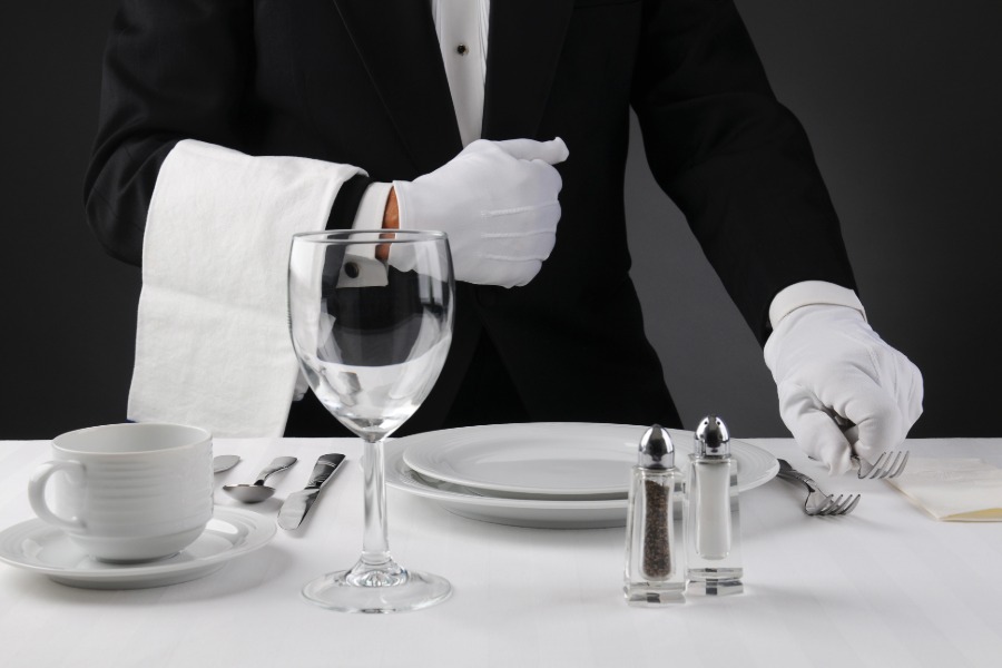 White-gloved catering employee arranging polished silverware